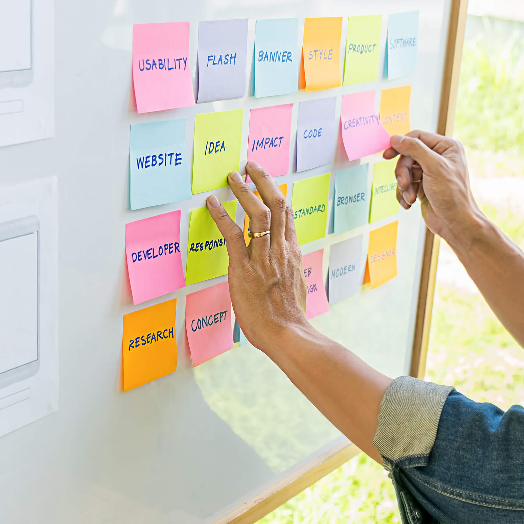 Hands organizing colorful sticky notes on a project board, representing agile execution and delivery.