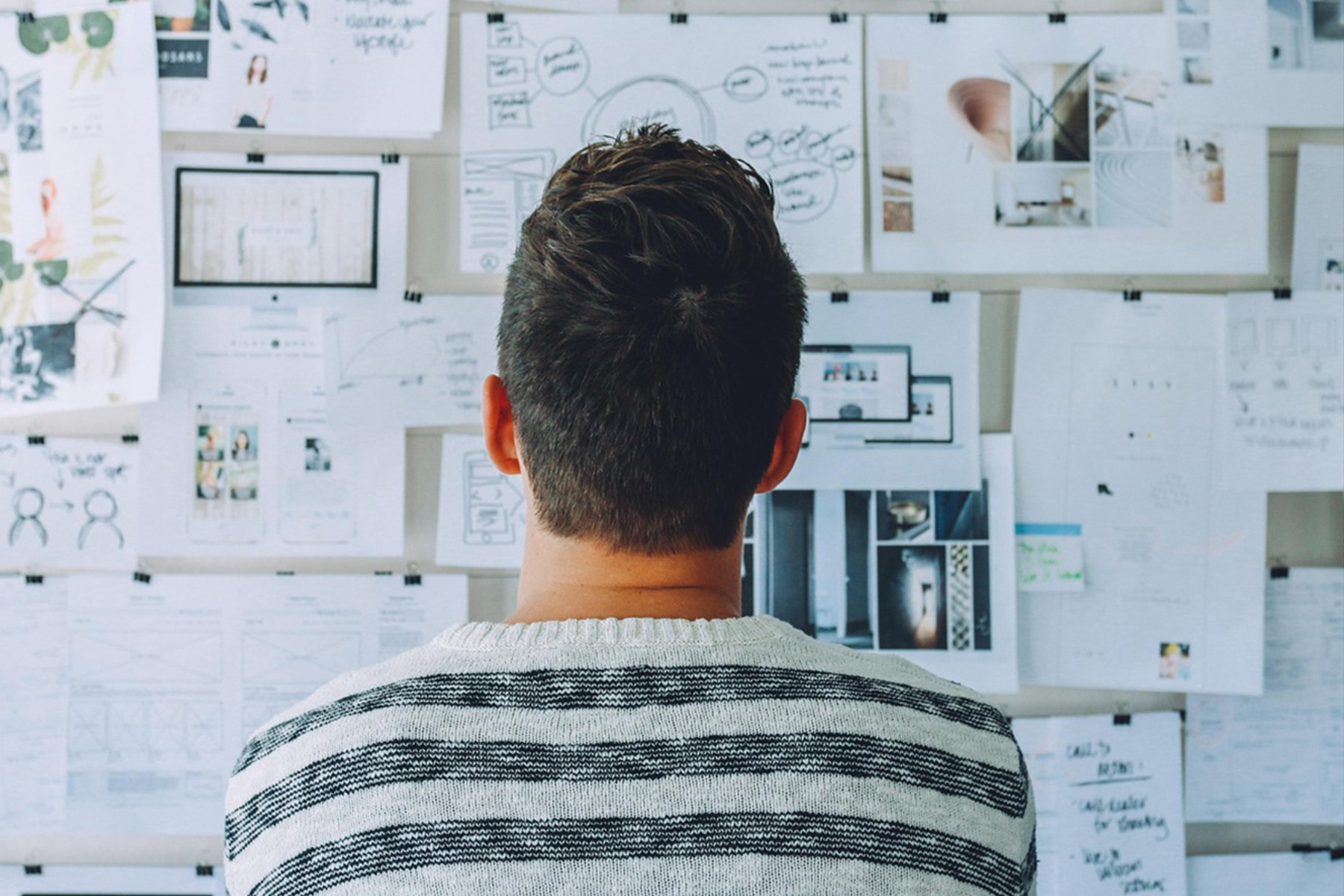 Person analyzing workflow charts and strategy plans pinned to a wall, representing automation planning and workflow design.
