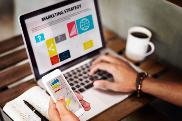 Person managing marketing strategy on laptop and smartphone, representing automated lifecycle campaigns and data-driven communication.