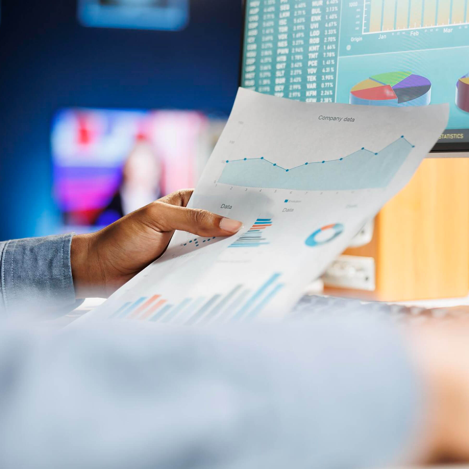 Person analyzing marketing data charts and system performance reports on screen and paper, representing automation and connected business workflows.